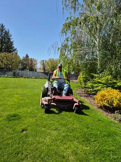 Tatum Lawn Care crew mowing beside a flower bed and willow tree in Moses Lake, WA