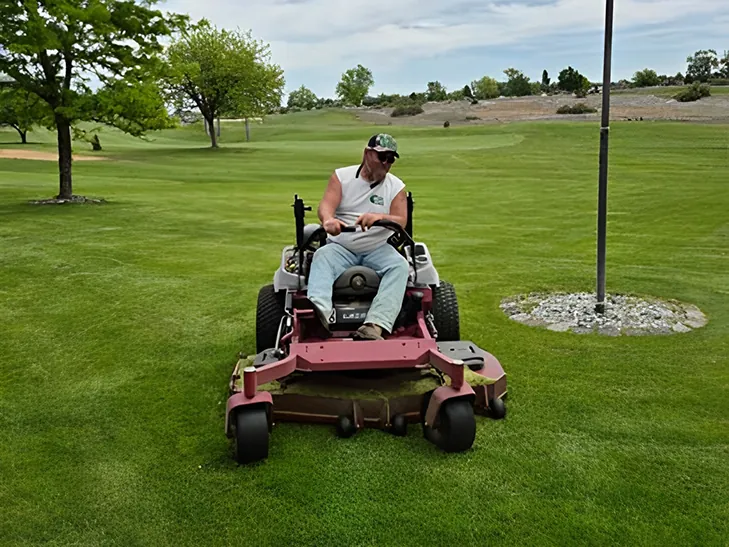 Tatum Lawn Care crew member on a zero-turn mower near a flagpole in Moses Lake, WA