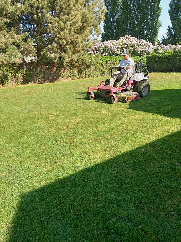Tatum Lawn Care crew mowing a backyard lawn with a zero-turn mower in Moses Lake, WA